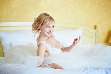 Cheerful young bride in wedding dress in hotel room