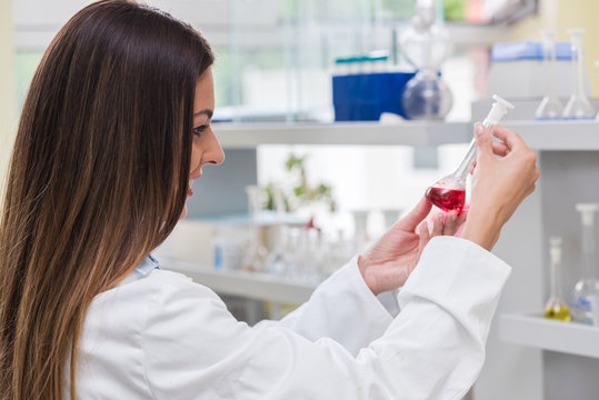 Woman scientist studying chemical liquid in lab flask. Scientist carrying out experiment in research laboratory