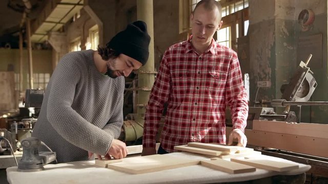 Footage in slowmotion of two young male carpenters dimensioning wooden workpieces in joinery
