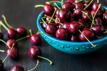 red cherries in green ceramic bowl on dark background