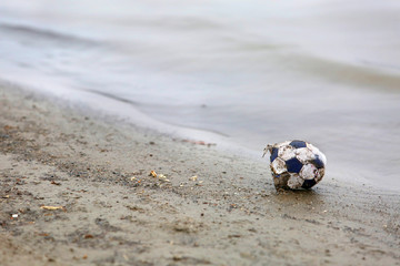 Ripped soccer ball on river coast