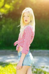 Obraz premium Beautiful young blonde woman with denim shorts and checked shirt enyoing in the park