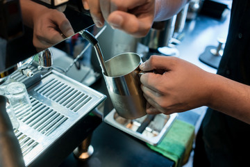 Hand of a barista holding a stainless mug while using a modern coffee machine