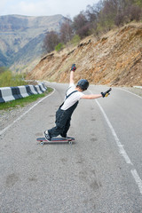 Longboarder on longboard in overalls helmet and gloves performs a stand-up slide at speed while on a mountain road serpentine in the mountains against the backdrop of a beautiful mountain landscape