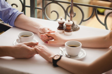 enamored couple holding their hands in the cafe, close-up