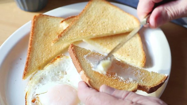 A man adds butter to his toast and fried eggs breakfast