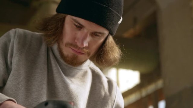 Close up footage of concentraed Caucasian young male with beard using sander in joinery. Footage in slowmotion