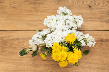 Bouquet of blossoming white lilac and yellow dandelions with foliage on an old wooden table, top view
