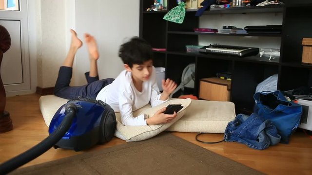 Boy teenager is shirking her homework, playing on her mobile phone. Cleaning of the children's room. Disorder in the teen room