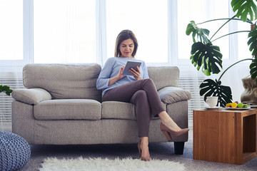 Fototapeta premium Concentrated adult female working in laptop while sitting on sofa