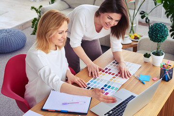 Fototapeta premium Smiling females working with catalog of color palette and laptop