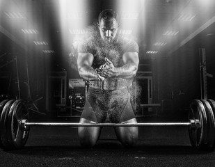 Ahlete kneels in the gym and claps his hands after which the dust from the chalk flies