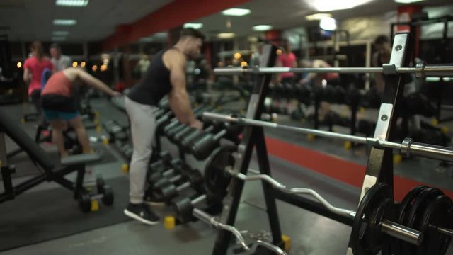 Fit guy approaching dumbbell stand and taking big fixed-weights to do exercises