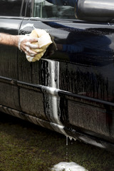 Dłoń mężczyzny zmywa bród z drzwi samochodu za pomocą gąbki z dużą ilością piany.