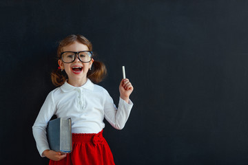 Happy schoolgirl preschool girl with book near school blackboard