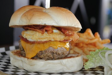 Big single cheeseburger with french fries  A serving of cheeseburger complete with eggs, bacon, ham and french fries 