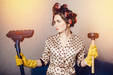 girl in a dressing gown with curls on her head curlers holds a plunger and a brush from a vacuum...