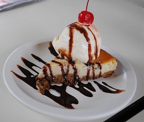 Cheesecake topped with ice cream and cherry A slice of cheesecake served with a scoop of icecream and cherry and sprinkled with chocolate syrup