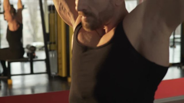 Male athlete doing rear lat pull-downs in gym with big efforts, face strained 