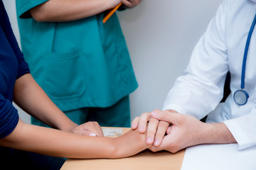 Friendly male doctor hand holding patient hand sitting at the desk for encouragement - empathy - cheering and support while medical examination.