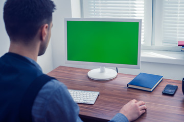 Young man office worker sitting at his desk working at computer with Chromakey on monitor. Office concept with working environment