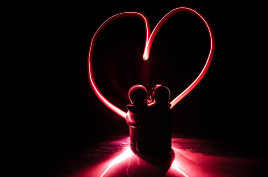 Two young lovers paint a heart on fire. Silhouette of couple and Love words on a dark background