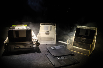 Pile of black floppy disks on dark background with light. Vintage computer attributes