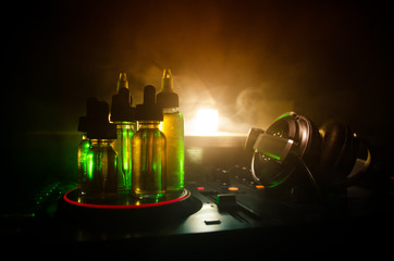 Vape and DJ Club concept. Smoke clouds and vape liquid bottles on Dj mixer close up. Light effects....