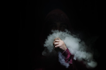 Vaping man holding a mod. A cloud of vapor. Black background. Vaping an electronic cigarette with a...