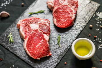 Rib eye beef cow steak meat with spices and herbs against black background