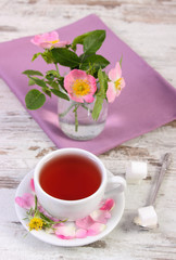 Cup of tea and wild rose flower on rustic wooden background