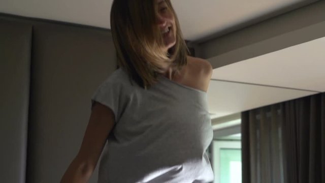 Happy, pretty woman jumping on bed at home, super slow motion 240fps
