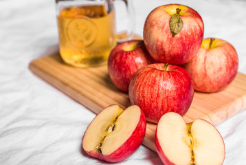 Red and pink apples and apple juice on a wooden board against white background