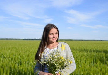 Naklejka na ściany i meble Young beautiful girl with a bouquet of chamomiles. A woman in a barley field