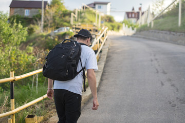 Tired young man with a backpack walks alone on a mountain road up the slope