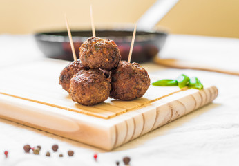 Meatballs on a wooden board with toothpicks against white background