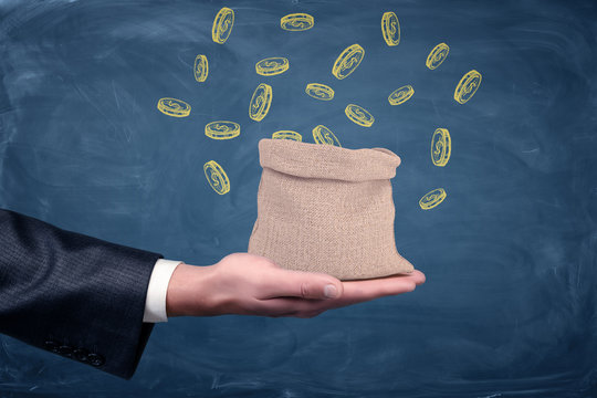 A businessman's hand turned up and a small money bag standing on it with drawn coins on blue background.