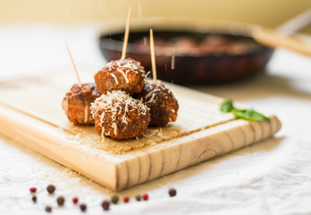 Meatballs in tomato sauce, cheese falling over them, on a wooden board with toothpicks against white background