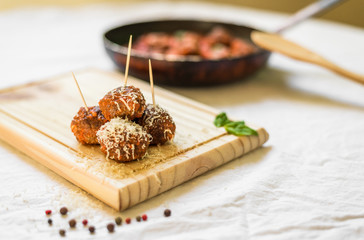 Meatballs in tomato sauce, cheese falling over them, on a wooden board with toothpicks against white background