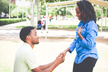 Portrait of young man dropping on knees to propose and lady answering i do, isolated outdoors...