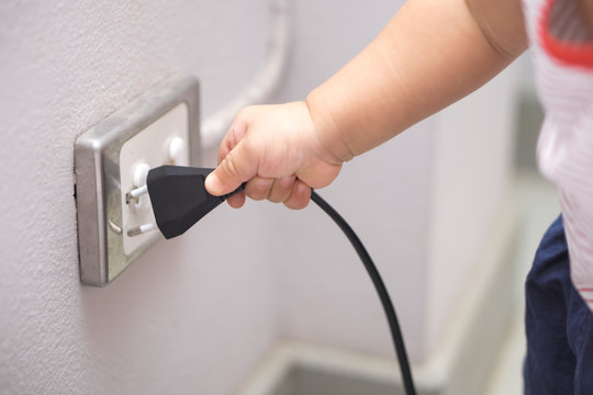 Hand of a baby trying to insert plug into electrical outlet covered with safety plugs