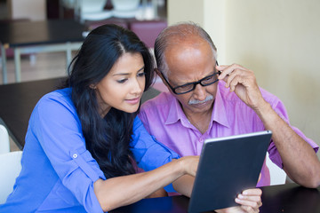 Closeup portrait, sitting young woman showing elderly with black glasses to use portable device,scrutinizing data with great concern, isolated indoors background