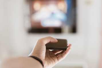 Closeup on hand holding smartphone and use a app with remote control and surfing programs on television in selective focus.