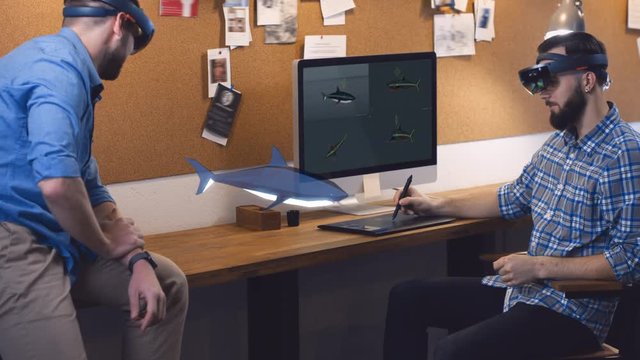 Young adult Caucasian colleagues using holographic augmented reality glasses together, discussing shark model hologram. Game development. 4K UHD RAW edited footage