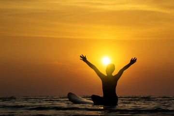 Fototapeta na wymiar Silhouette of surf man sit on a surfboard, open arms. Surfing at sunset beach. Outdoor water sport adventure lifestyle.Summer activity. Handsome Asia male model in his 20s.