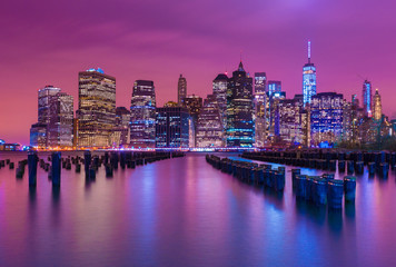 Manhattan skyline at night with varicolored reflections in the water, view from Brooklyn, New York, USA