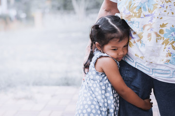 Sad asian little girl hugging her mother leg in vintage color tone