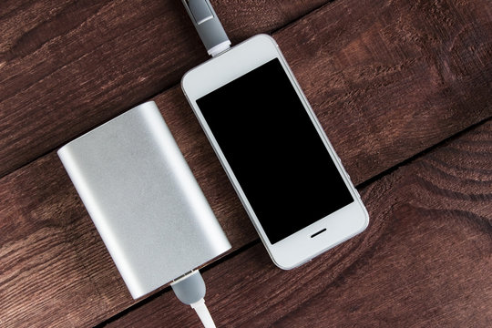 Grey Phone And Power Bank Connected By Cord On Wooden Desk