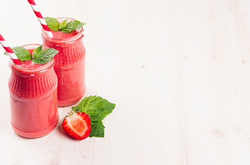 Freshly blended red strawberry fruit smoothie in glass jars with straw, mint leaf, cut ripe berry....