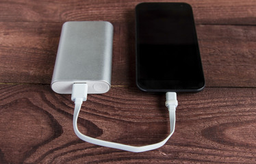 Charging smartphone with grey portable external battery on wooden table